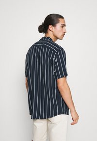 Marineblaues Kurzarmhemd mit weißen vertikalen Streifen, einem Button-Down-Kragen und einer lässigen Passform, gefertigt aus leichtem Stoff.