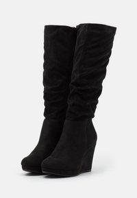 Botas de cuña altas de ante negro con un diseño arrugado, punta redondeada y cremallera lateral, que presentan una textura suave y una silueta elegante.
