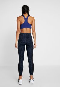 Top sportivo di colore blu profondo, con design a schiena scoperta. Leggings neri aderenti con stampa leopardata scura. Indossato con sneaker bianche.