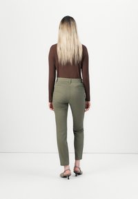 Olive green fitted pants with a smooth texture and back pockets, paired with a ribbed brown long-sleeve top. Minimalist style.