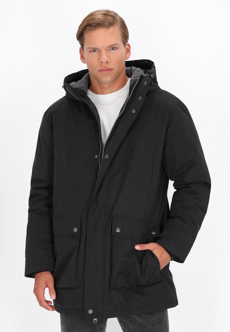 Zwarte parka met een rits en drukknoopsluiting, grijze voering, capuchon en twee voorzakken met klep. Heeft een relaxte pasvorm en een soepele textuur.