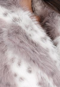 Faux fur wrap i blød pastelllilla med hvide pletter, der har en luksuriøs tekstur og et voluminøst design, perfekt til lagdeling.