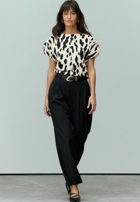 Haut à manches courtes avec un motif animal noir et crème, associé à un pantalon noir taille haute et une boucle de ceinture dorée, le tout sur un fond neutre.