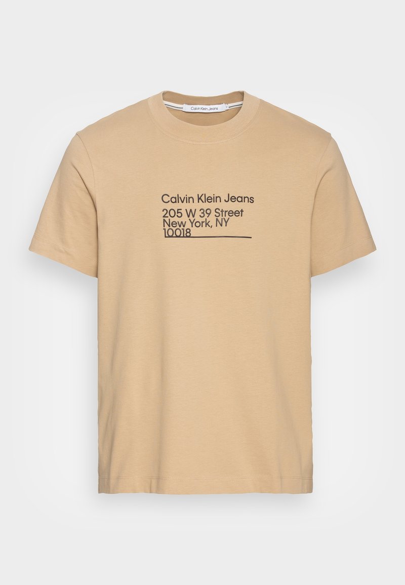 Beige bavlněné tričko s krátkým rukávem. Na přední straně je černý text: "Calvin Klein Jeans," adresa a PSČ.