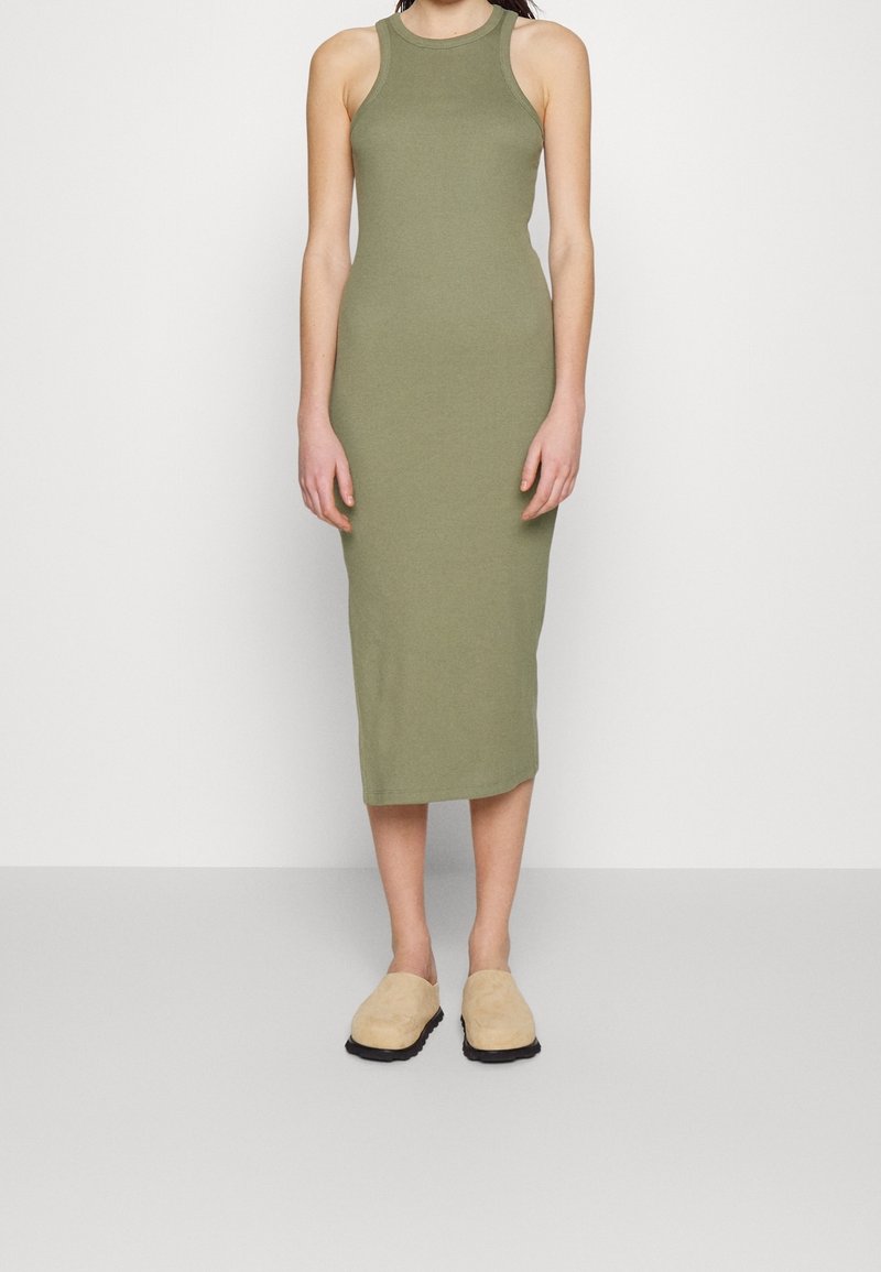 Olivgrünes, ärmelloses Midikleid mit taillierter Passform. Glatte Textur und runder Ausschnitt. Kombiniert mit beigen Slippers.