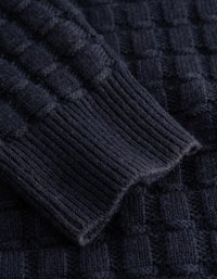 Suéter de malha azul-marinho em close-up, apresentando padrões texturizados e punhos canelados, exibindo um tecido suave e uma trama detalhada.