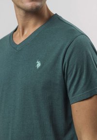 Grønn V-hals t-skjorte laget av mykt stoff, med korte ermer og en liten logo på brystet. Glatt tekstur med en avslappet passform.