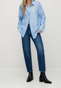 Błękitna, luźna koszula na guziki z długimi rękawami, zestawiona z ciemnymi jeansami o prostych nogawkach i czarnymi botkami za kostkę.