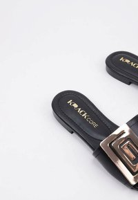 Chanclas negras con textura suave, presentan un brillante hebilla cuadrada dorada y una plantilla con marca, diseñadas para un uso de dedo abierto.