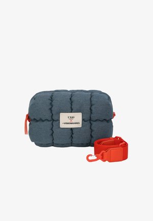 Blue padded fabric bag with a silver logo plate, featuring a red detachable strap. Rectangular shape with textured surface and bold accents.