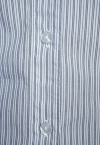 Chemise à col boutonné avec des rayures verticales en bleu clair et marine foncé. Elle dispose d'un bouton en plastique transparent et d'une texture de tissu lisse.