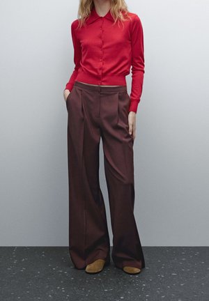 Red fitted cardigan with a collar and buttons paired with high-waisted, wide-leg dark brown trousers. Soft fabric and structured shape.