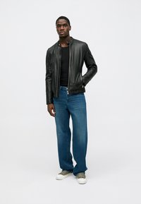 Mustast nahast bomber-tüüpi jakk sileda viimistlusega, lukuga ja soonikkoes äärega, kombineeritud siniste teksapükste ja hallide tossudega.