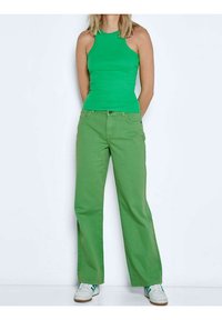 Zelený top na ramínka spárovaný s rovnými zelenými kalhotami. Obě vyrobeny z hladké látky. Bílé tenisky se zelenými akcenty doplňují celý outfit.