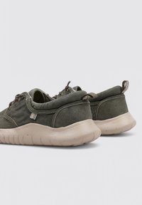 Zapatillas verde oliva de tejido suave con suela de goma beige, forma redondeada, cordones mínimos y un pequeño logotipo acentuado en el lateral.