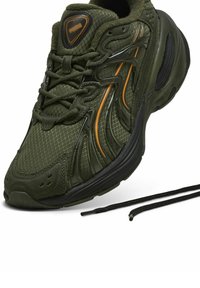 Olajzöld sportcipő hálós és szintetikus anyagokból, texturált felülettel, narancssárga részletekkel, fekete talppal és fekete fűzővel.