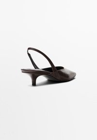 Chaussure slingback en cuir marron avec un bout pointu, un petit talon et une sangle courbée. Texture lisse avec des détails de couture subtils.