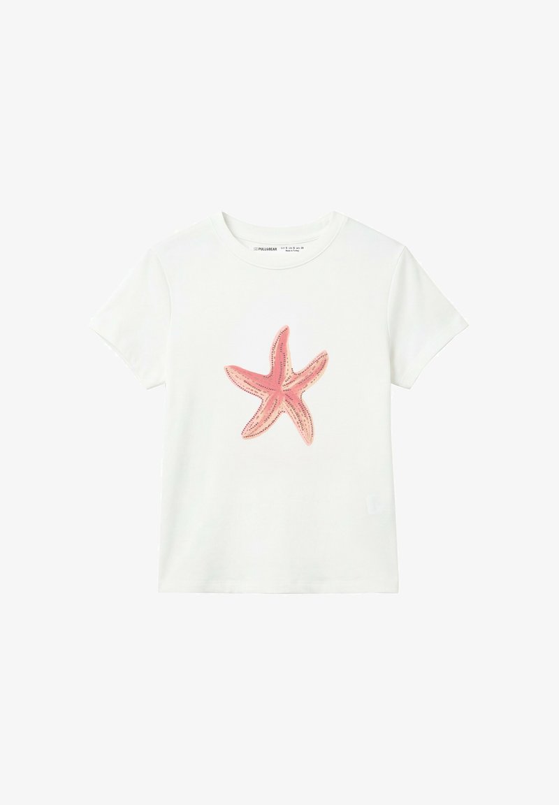 T-shirt blanc à manches courtes avec un grand motif d'étoile de mer rose au centre sur un fond uni.