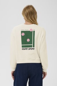 Felpa color crema con taglio corto, decorata con una grafica verde di palline da tennis, la scritta "Saint Tropez '86" e "COURT SPORT".