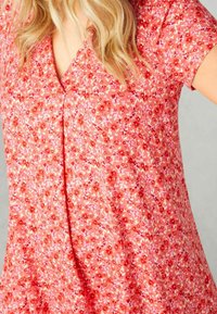 Vestido de flores rojas con manga corta, escote en V y tejido ligero que presenta acentos en rosa y blanco. Textura suave y diseño liviano.