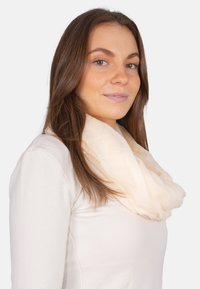 Leichter beiger Schal mit einer weichen, durchsichtigen Textur, um den Hals drapiert, der zu einem Langarmoberteil passt.