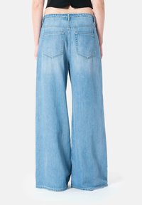 Wide-leg, light blue denim jeans with a high waistband, two back pockets, and a soft texture. Raw hem at the bottom edge.