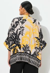 Kimono léger en crème, avec de grands motifs floraux noirs et jaunes, une bordure géométrique noire, des manches larges et une coupe décontractée.