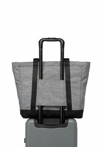 Sac fourre-tout gris attaché à la poignée déployée d'une valise à roulettes grise avec finitions et sangles noires.