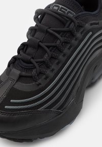 Svart idrottssko med en ovandel i mesh med grå ränder, texturerade snören och en robust sula med subtila detaljer.