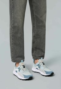Zapatillas con un diseño multimaterial en azul claro y gris, que presentan paneles texturizados, acentos en negro y suelas de goma. Llevadas con jeans rectos.