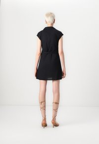 Vestido preto de manga curta com cintura cingida e decote com gola. O tecido parece suave e leve. Sandálias de salto alto de tiras em tom bege.