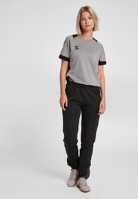 Grijze sportshirt met zwarte accenten, gecombineerd met zwarte joggers. Heeft een elastische tailleband en ademend materiaal met gestructureerde details.