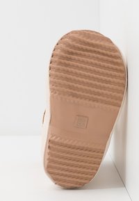 Beżowa podeszwa sneakersów z teksturowanym gumowym gripem, z subtelnym wzorem i wyraźną cyfrą "22" wytłoczoną na matowej powierzchni.