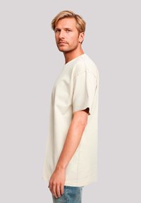 Beige katoenen t-shirt met een ontspannen ontwerp, korte mouwen en een ronde hals, gepresenteerd tegen een neutrale achtergrond.