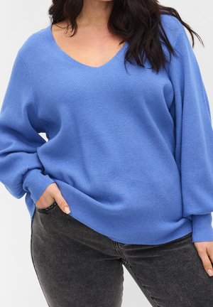 Blauwe gebreide trui met een v-hals en een relaxte pasvorm. Heeft lange mouwen en een geribbelde textuur. Gepaard met donkergrijze jeans.