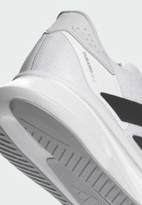 Weiße Sportschuhe mit strukturiertem, atmungsaktivem Obermaterial und schwarzem Streifen an der Seite. Dicke Gummisohle mit detaillierten Mustern für besseren Halt.