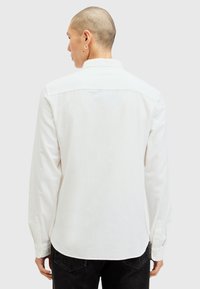 Hvid langærmet skjorte med krave, knapmanchetter og buet kant. Fremstillet af blødt stof, med minimalistisk design, ingen mønstre eller grafik.