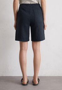 Marineblauwe linnen shorts met een relaxte pasvorm, voorzien van een elastische tailleband en een enkele achterzak, die net boven de knie eindigen.