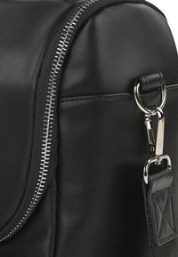 Bolso de cuero negro con un zipper metálico, herrajes plateados y un punto de sujeción texturado. Superficie lisa con costuras detalladas.