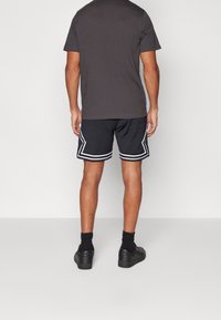 Pantalones cortos deportivos negros con acentos blancos, combinados con una camiseta gris oscuro. Los pantalones cortos presentan un diseño deportivo y una ligera textura. Se llevan calzado negro.