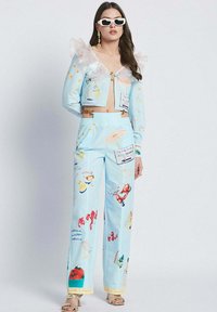 Blue cropped jacket with ruffled transparent sleeves, paired with blue patterned wide-leg pants featuring illustrations and colorful accents.