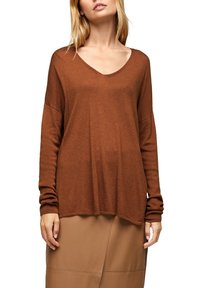 Pull en maille couleur rouille avec un col en V, des manches longues et une coupe décontractée. Porté sur une jupe marron clair lisse avec des coutures diagonales.