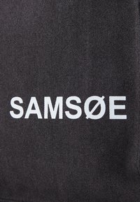 Black fabric tote with the brand name "SAMØSØ" in bold white letters. The texture is woven, giving a durable appearance.