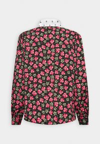 Blouse noire à manches longues avec motif floral rose, feuilles vertes, et col blanc contrastant à pois noirs, vue de dos.