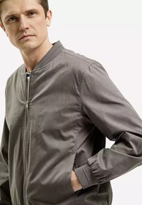 Szara kurtka bomberka zapinana na zamek z ribbowymi mankietami i bocznymi kieszeniami. Wykonana z gładkiego materiału, z delikatnym połyskiem i minimalistycznym wykończeniem.