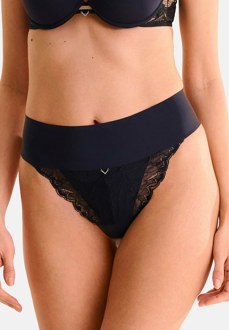 Ensemble de lingerie noire comprenant une taille lisse et des détails en dentelle. Le haut est un soutien-gorge avec armatures, et le bas est un string avec des motifs élaborés.