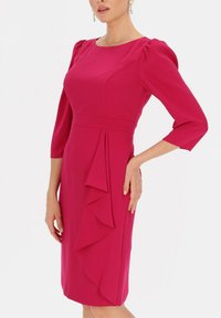 Fuksjowa sukienka z rękawami 3/4, dopasowanym korpusem i kaskadowym wykończeniem falbany na spódnicy, wykonana z gładkiego materiału.