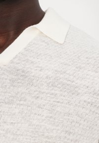 Lys beige strukturert strikkegenser med en flat, myk krage og et subtilt vevd mønster.