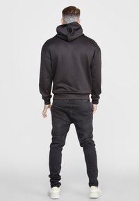 Sudadera negra con capucha, con una textura suave y un corte relajado, combinada con jeans oscure y zapatillas blancas.