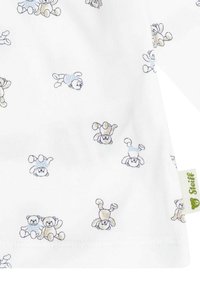 Weißer Stoff mit einem sich wiederholenden Muster von Teddybern in Hellbraun und Blau, mit einem kleinen grünen Etikett, das "Steiff" beschriftet ist.